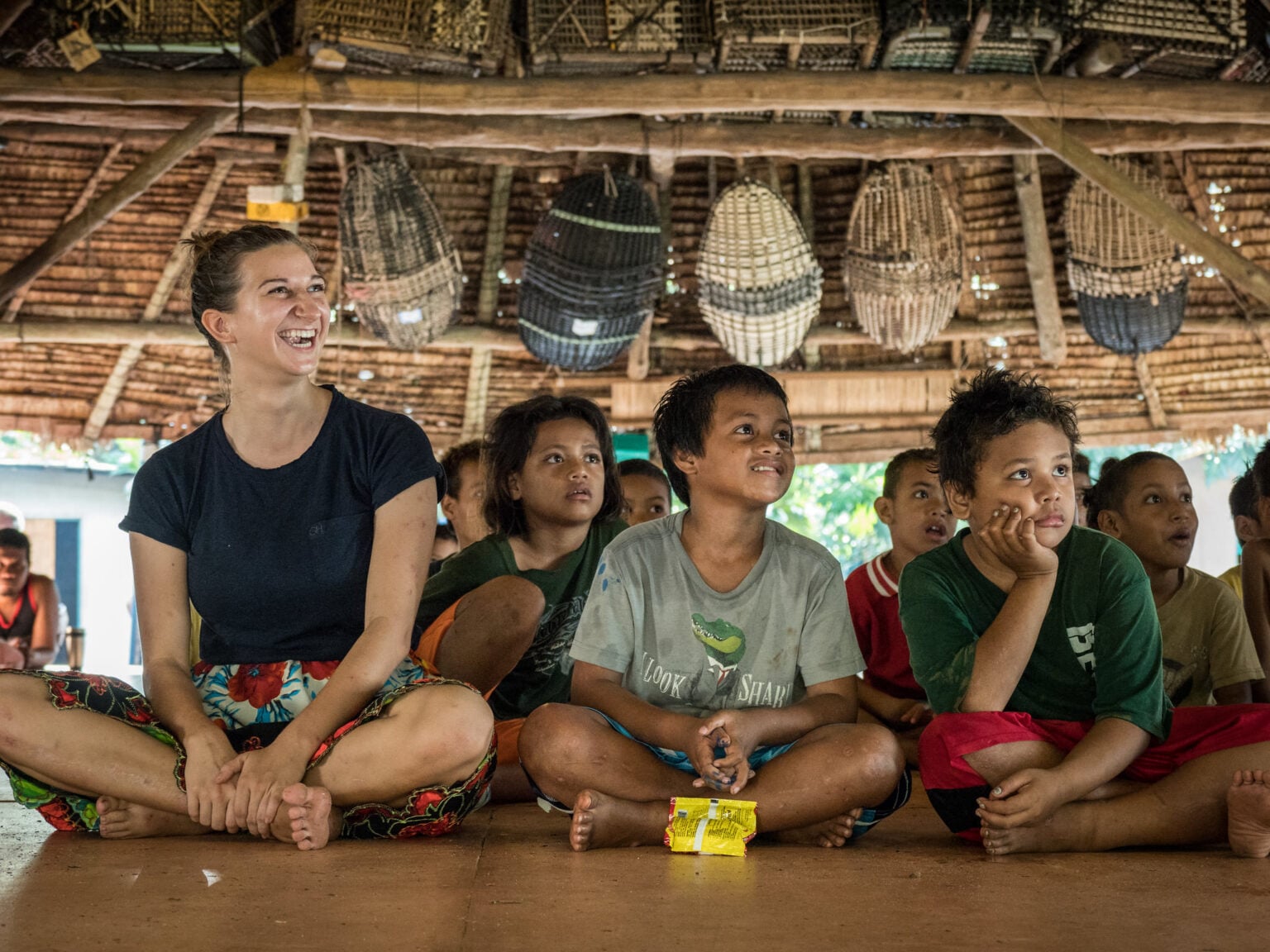 South Pacific school children and student missionary sitting on floor of bamboo building