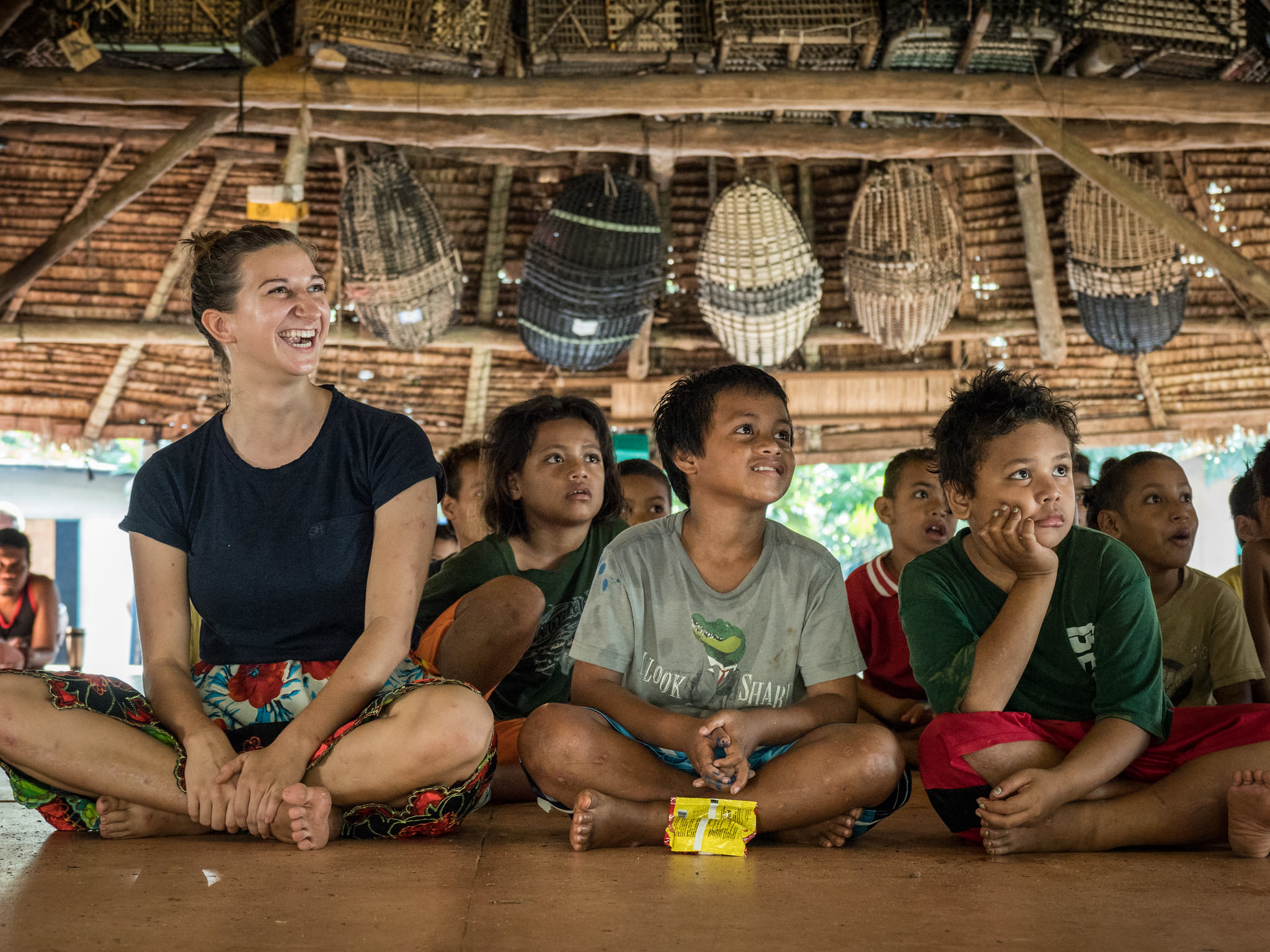 South Pacific school children and student missionary sitting on floor of bamboo building