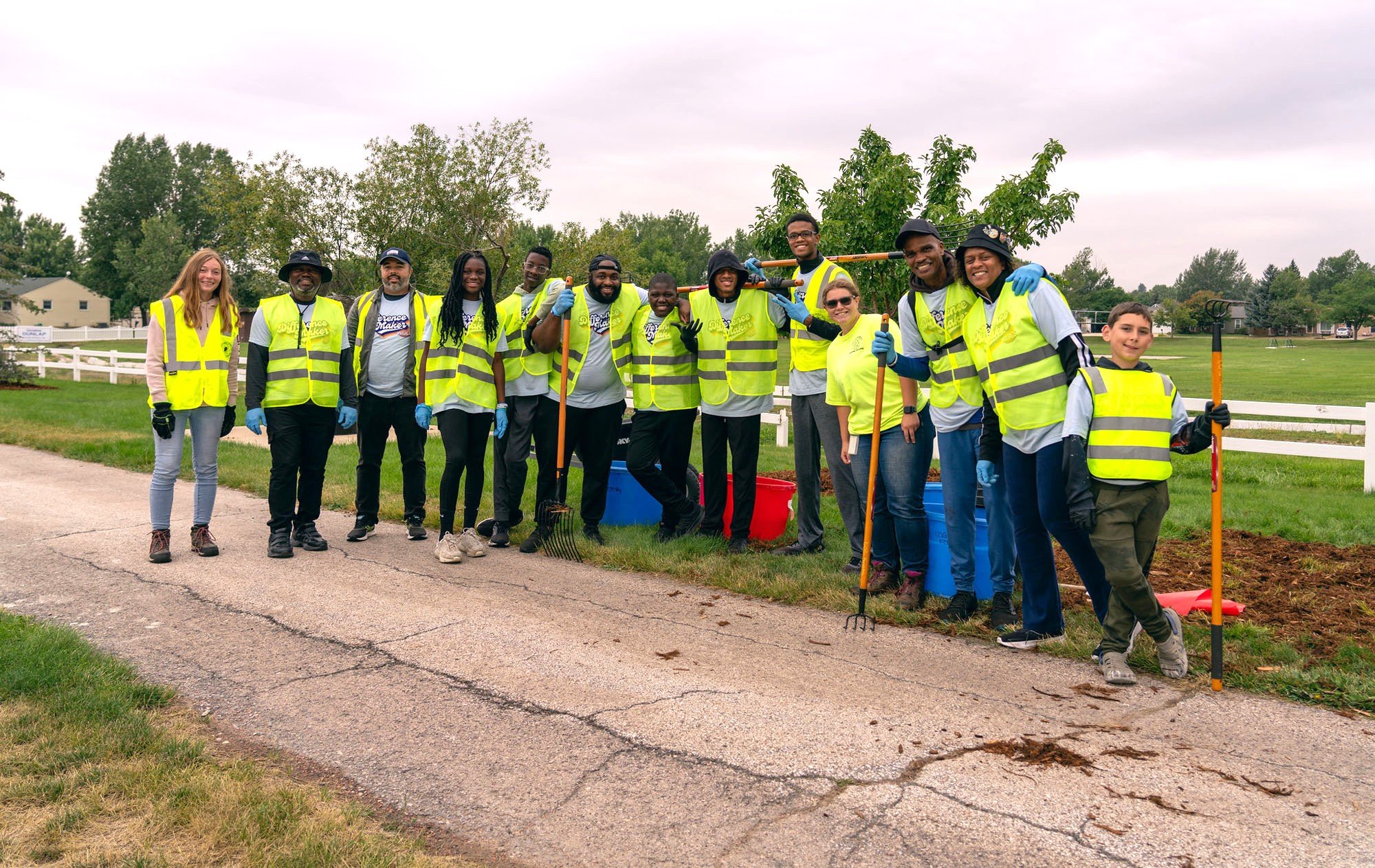 A group of volunteers in yellow reflector vests with gardening tools