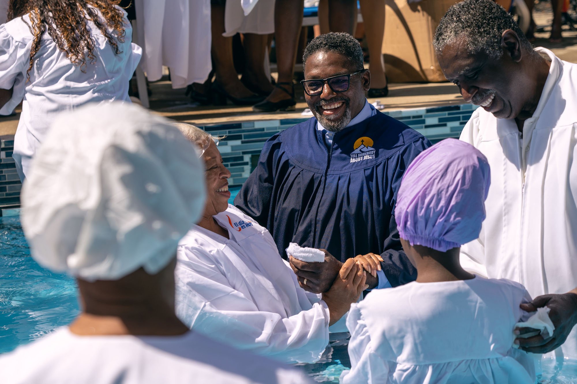 Smiling African-American minister and staff standing in a swimming pool about to baptise new converts