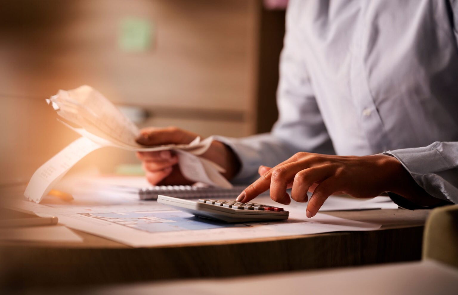 Hands of person using a calculator and holding financial receipts while sitting at a desk