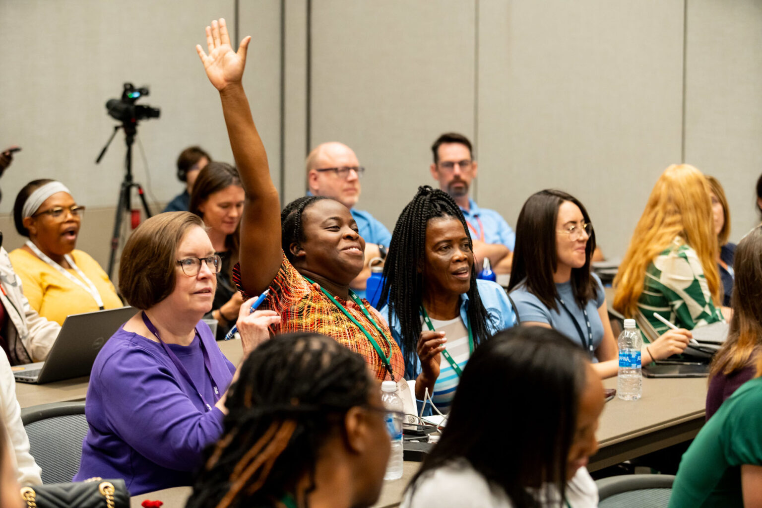 Group of adults in a classroom setting. One woman is eagerly raising her hand to answer a question.