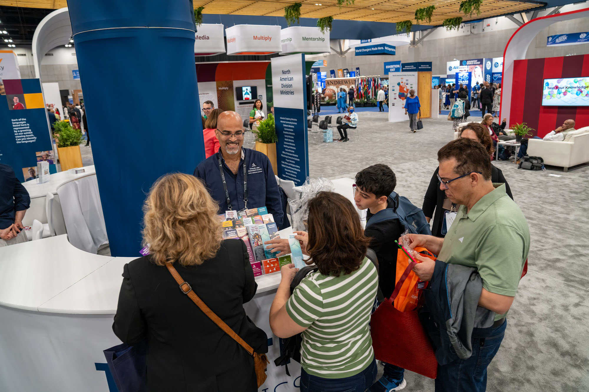 A group of people crowd around a booth inside an exhibit hall