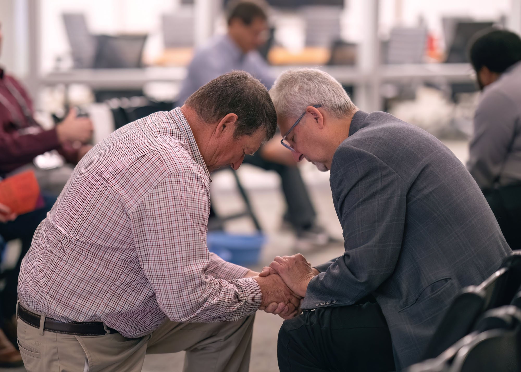 Two mean in business atire are kneeling face to face and praying together.