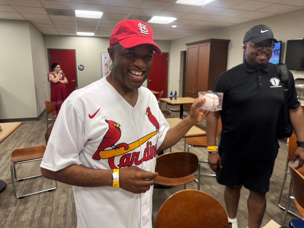 Middle age Black man in Cardinals shirt with baseball smiles