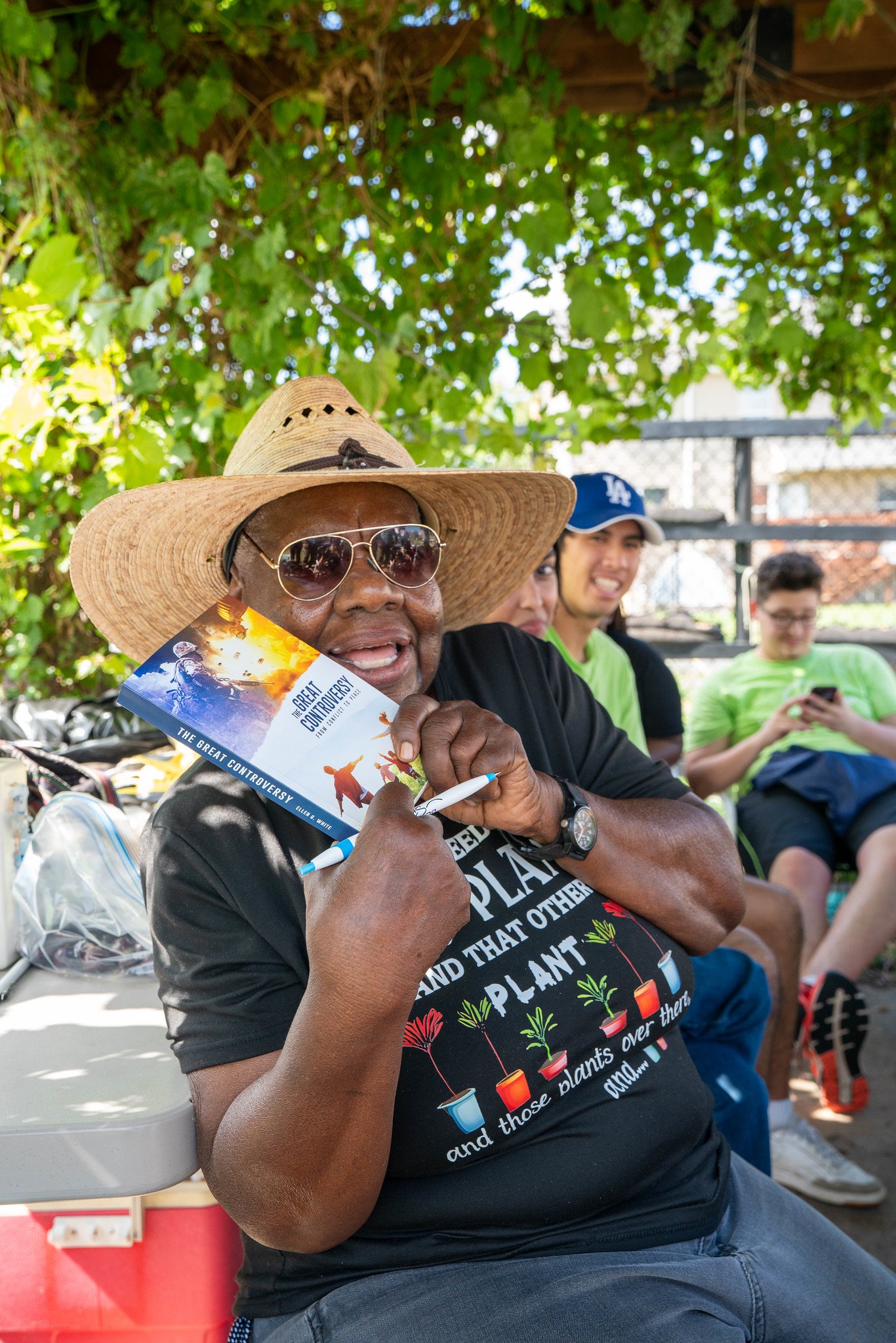 A smiling woman wearing a wide-brimmed hat holds a copy of The Great Controversy.