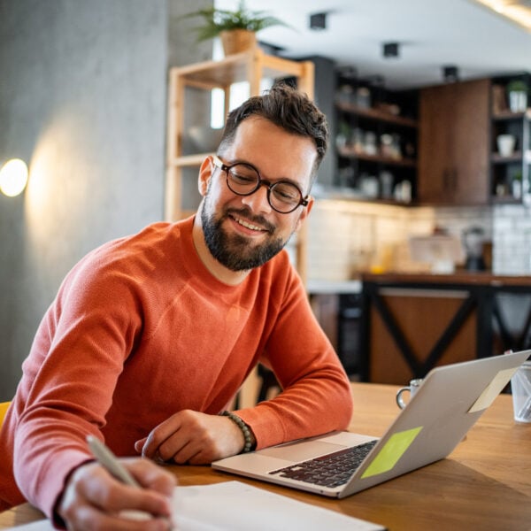 Man at home sitting at his kitchen table taking an online class on his laptop.