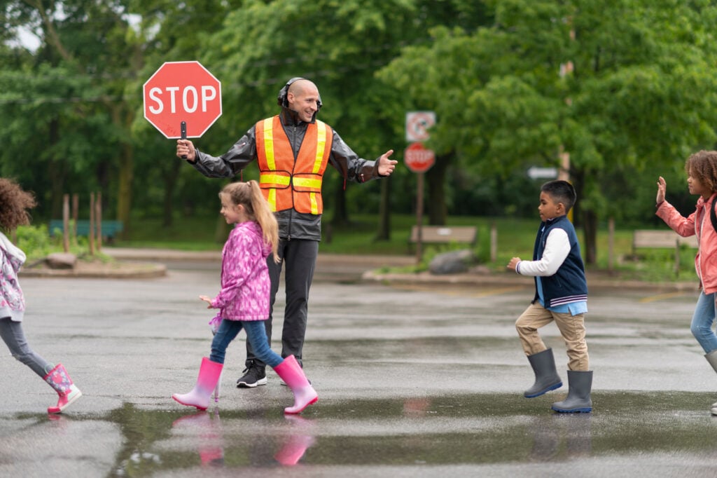 School crossing guard holds stop sign while children safely cross the road.