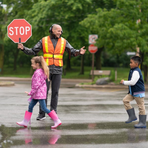 School crossing guard holds stop sign while children safely cross the road.