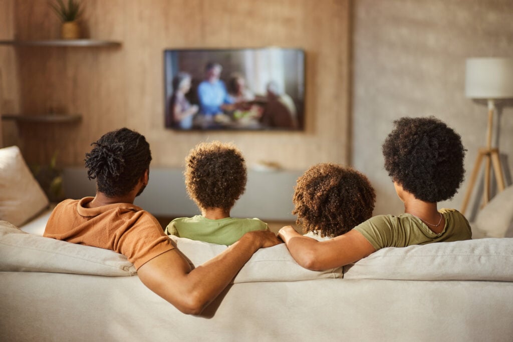 Back view of a black family watching TV at home.