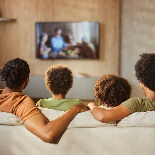 Back view of a black family watching TV at home.