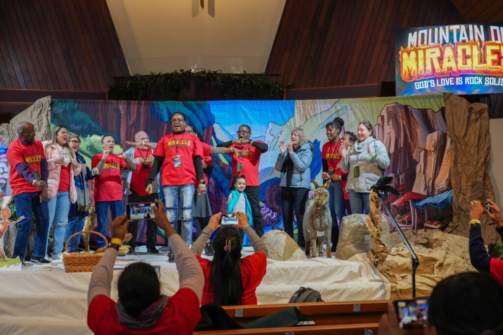 Group of adults onstage at a church in front of a colorful stage set for a children's Vacation Bible School.