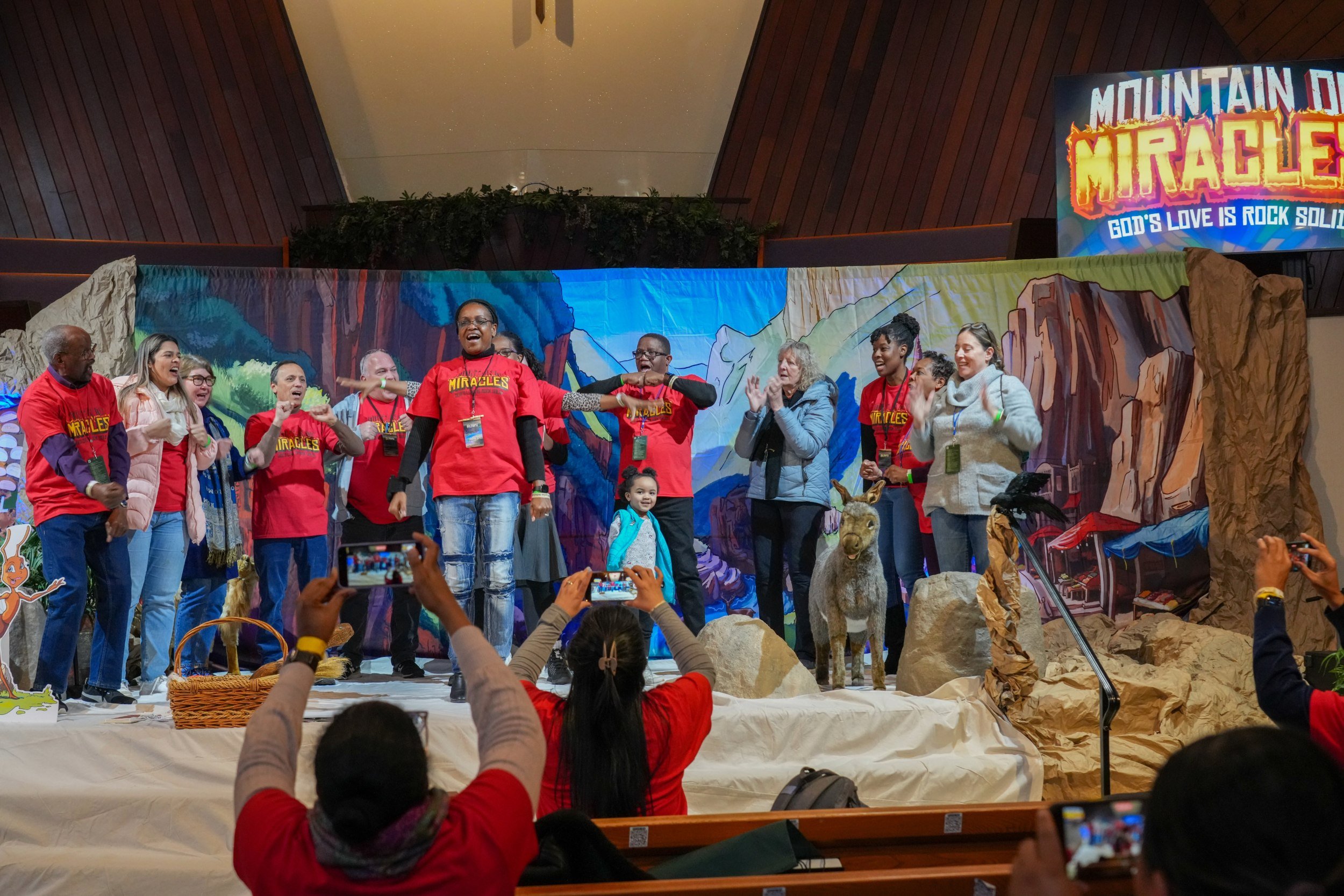 Group of adults onstage at a church in front of a colorful stage set for a children's Vacation Bible School.