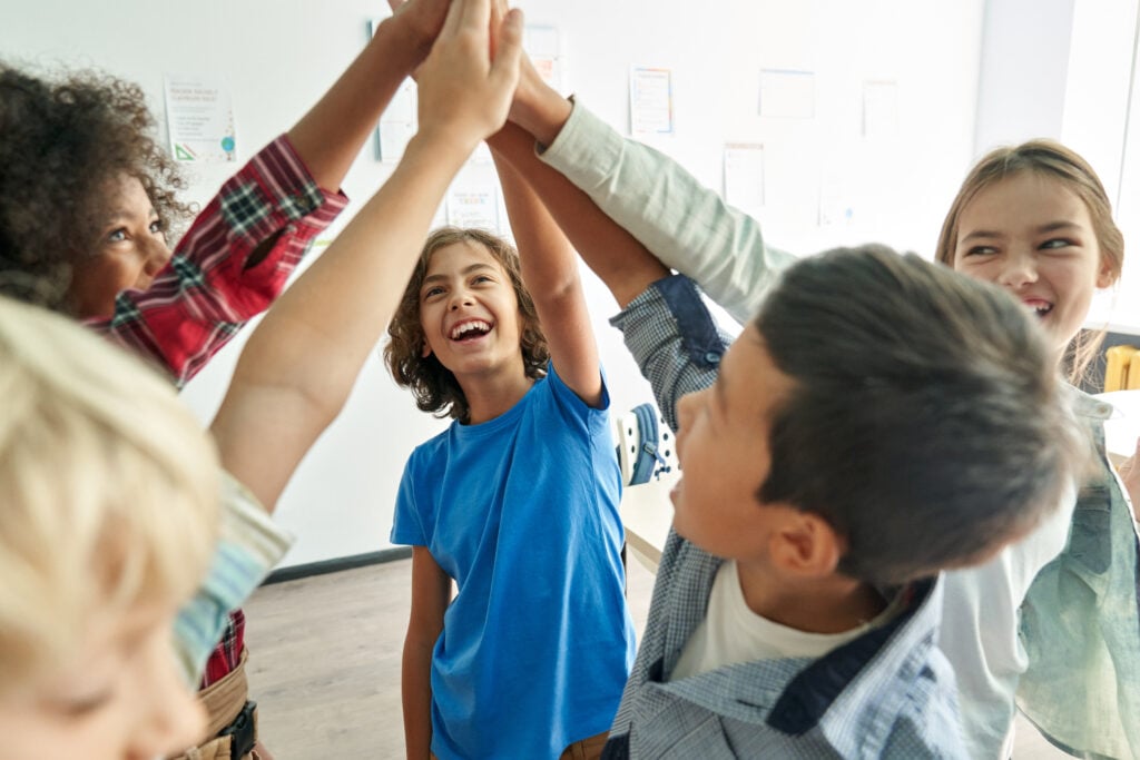 Photo of a group of children high fiving all together.