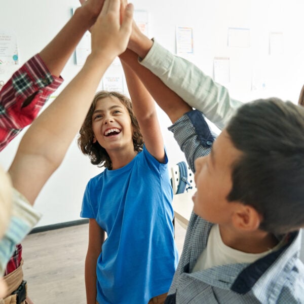 Photo of a group of children high fiving all together.