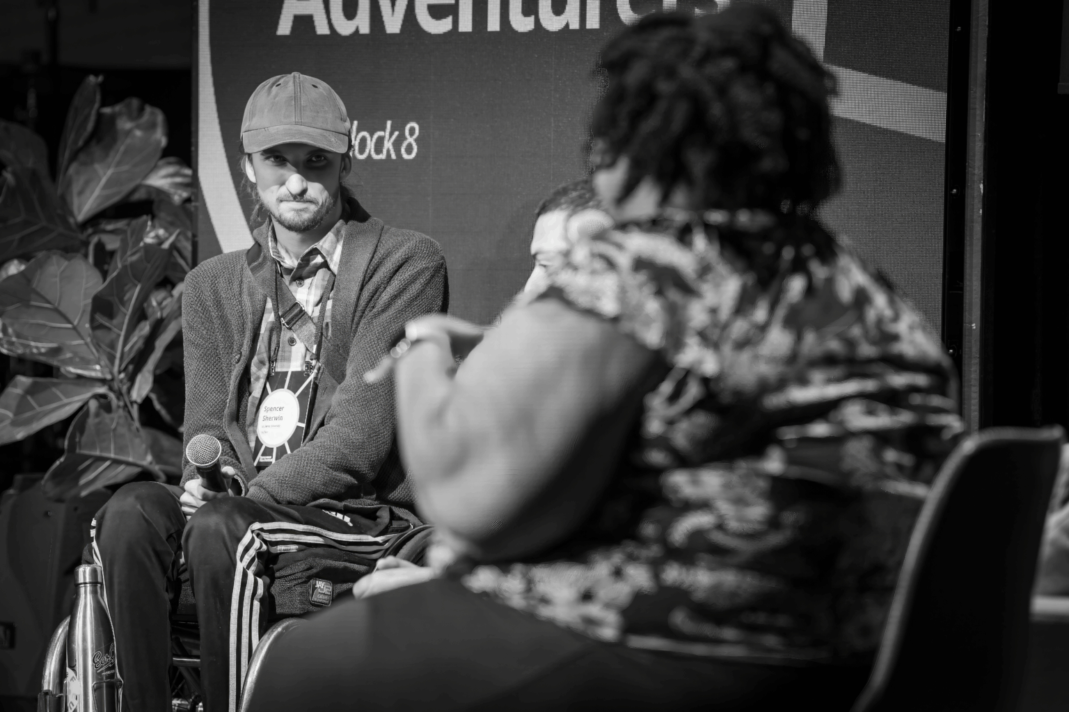 Young man in a wheelchair speaks to a woman on a stage