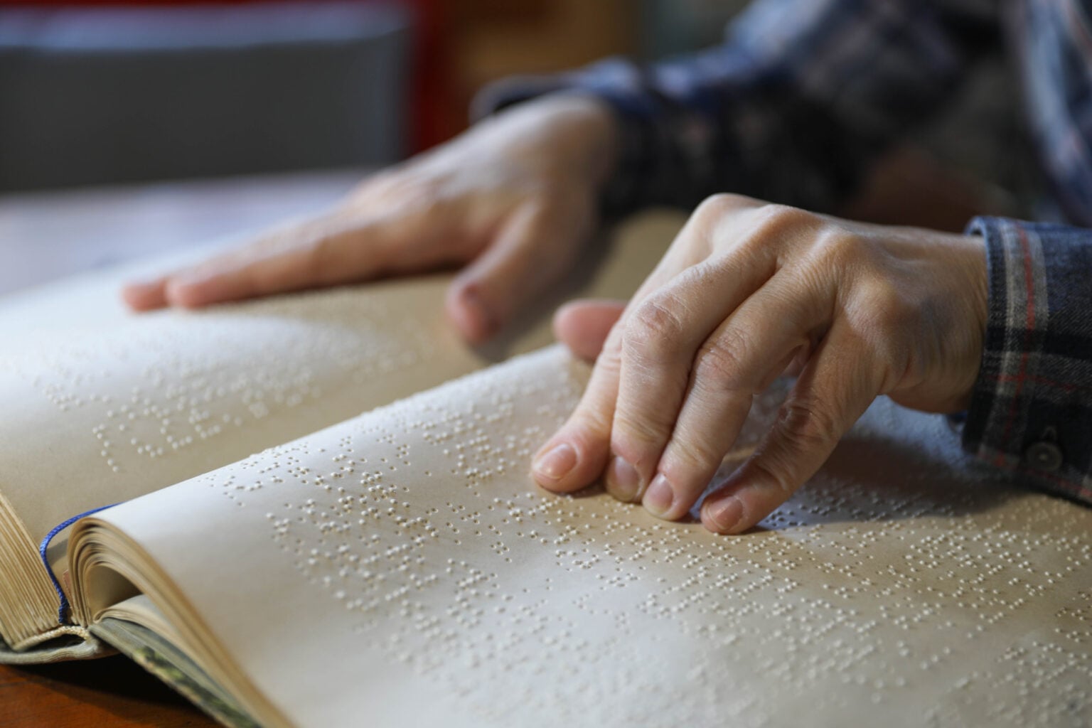 Photo showing two hands of a person who is reading braille type in a book.