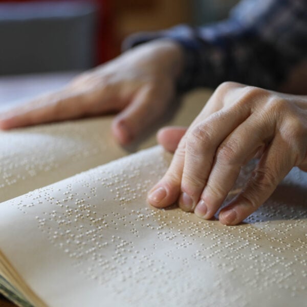 Photo showing two hands of a person who is reading braille type in a book.