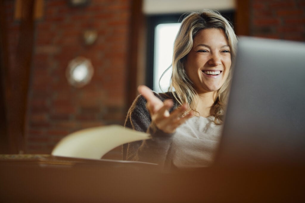 Happy young woman having a discussion with a person on her laptop screen.