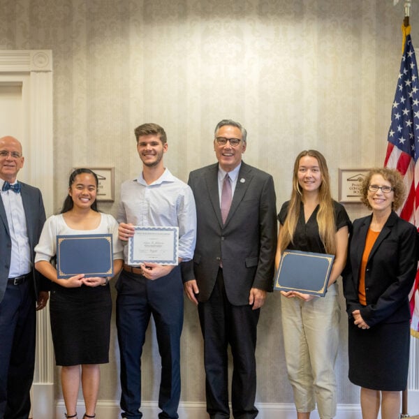 Three Southern Adventist University students stand alongside faculty with certificates, posed in front of the U.S. flag.