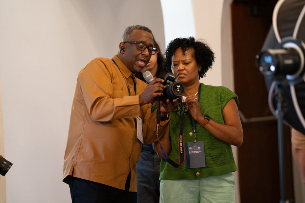 A man holding a mic shows a woman something on a camera. 