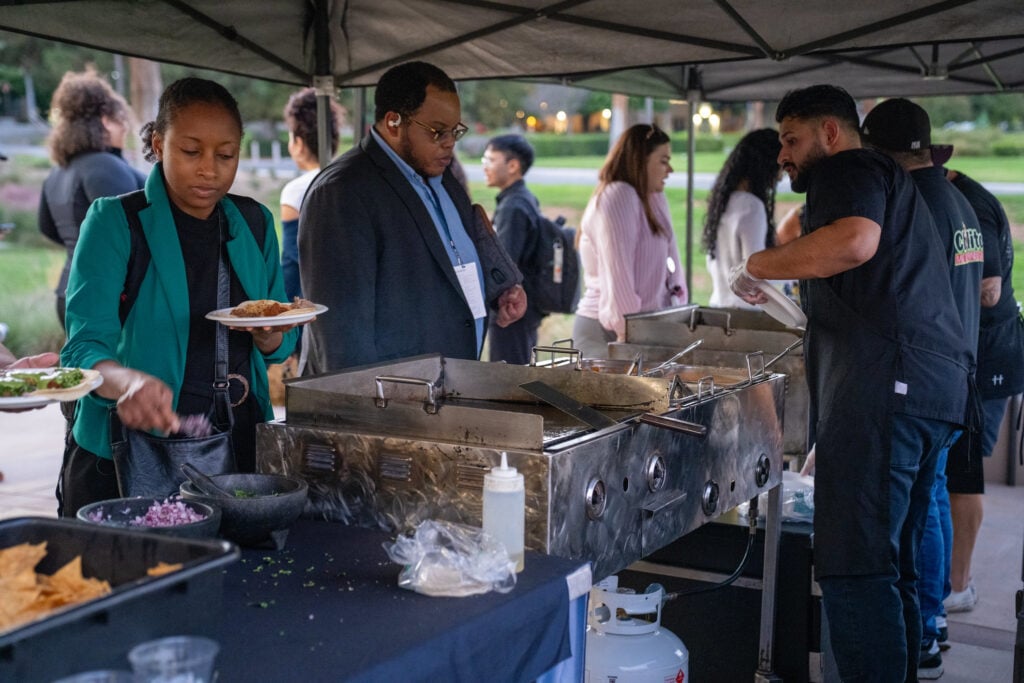 A diverse group of people assembling food at an outdoor taco dinner