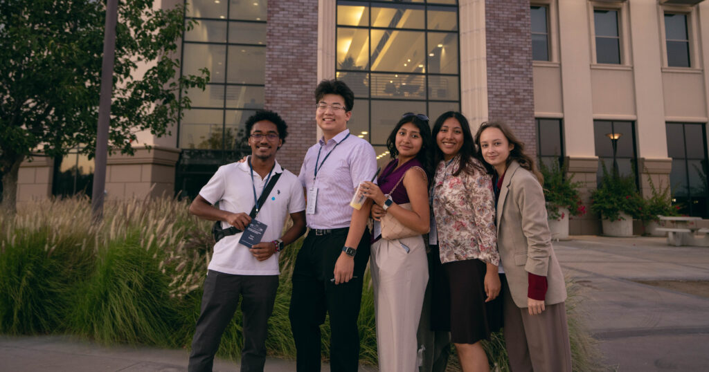 A diverse group of young people pose outside a university building. 