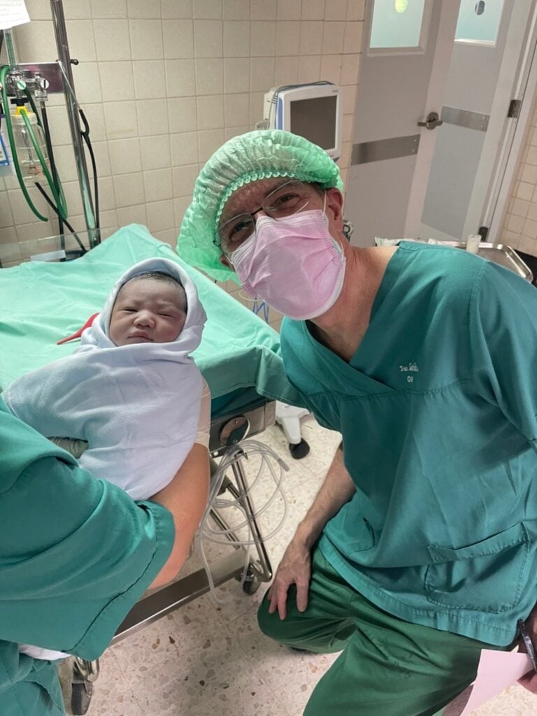 A physician  in green scrubs with a newborn baby in the hospital