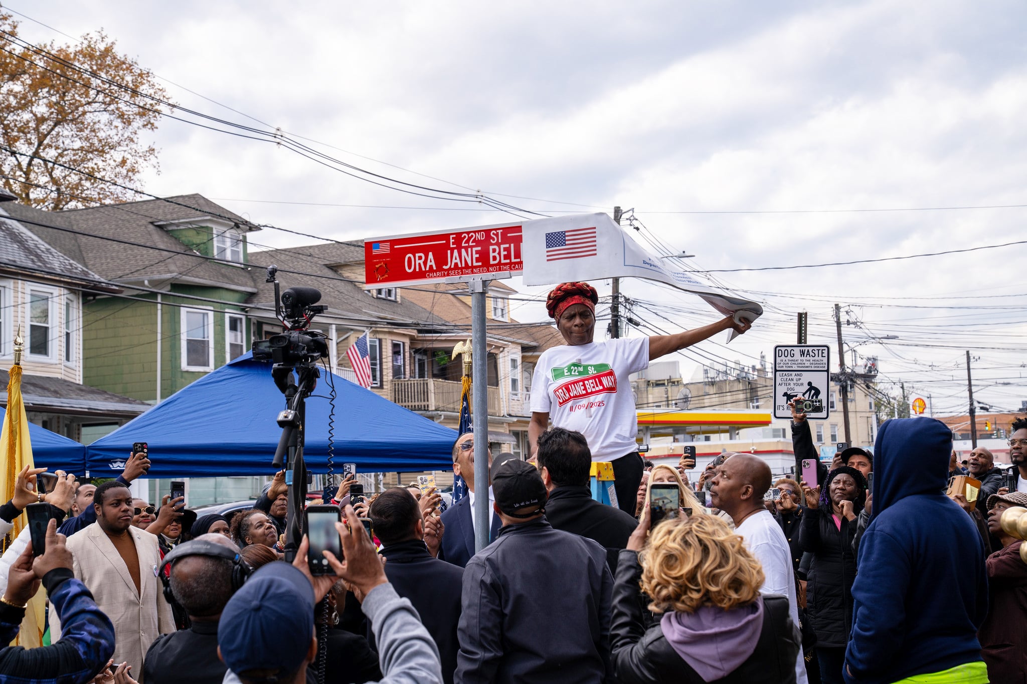 A woman unveils a new street sign as a crowd watches