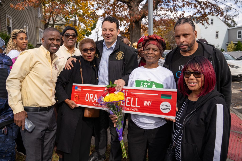 Group photo with several people holding a sign reading Ora Jane Bell Way. 