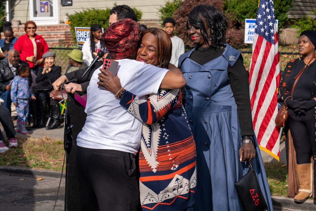 Two women embrace as another looks on. 