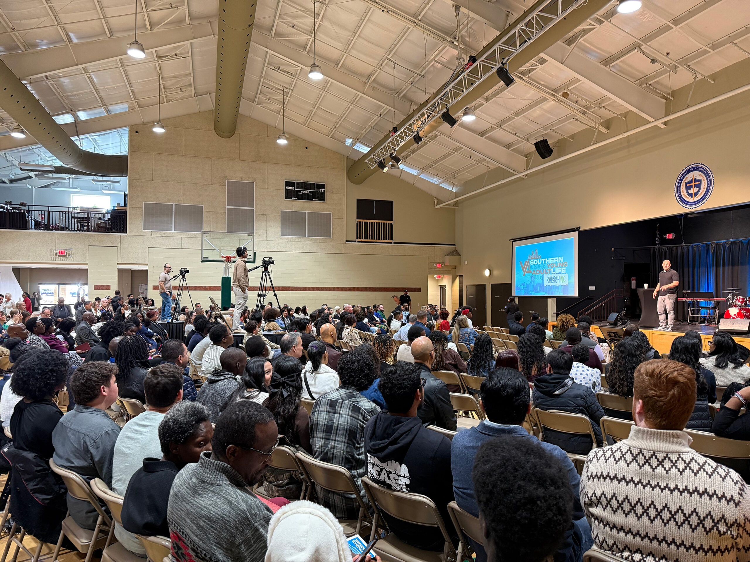 A speaker on a platform in front of a packed auditorium