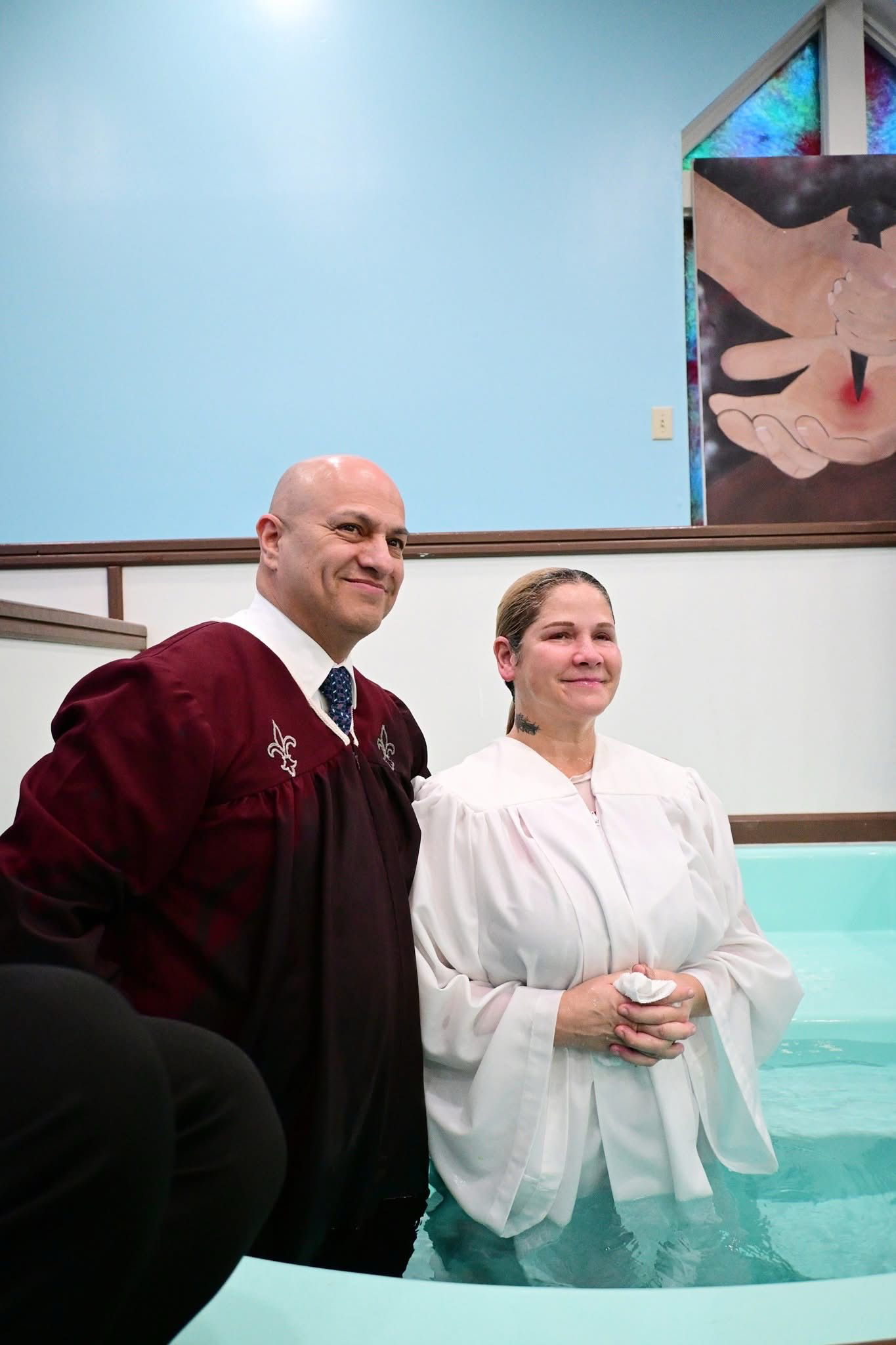A smiling woman and male pastor stand in the baptismal pool