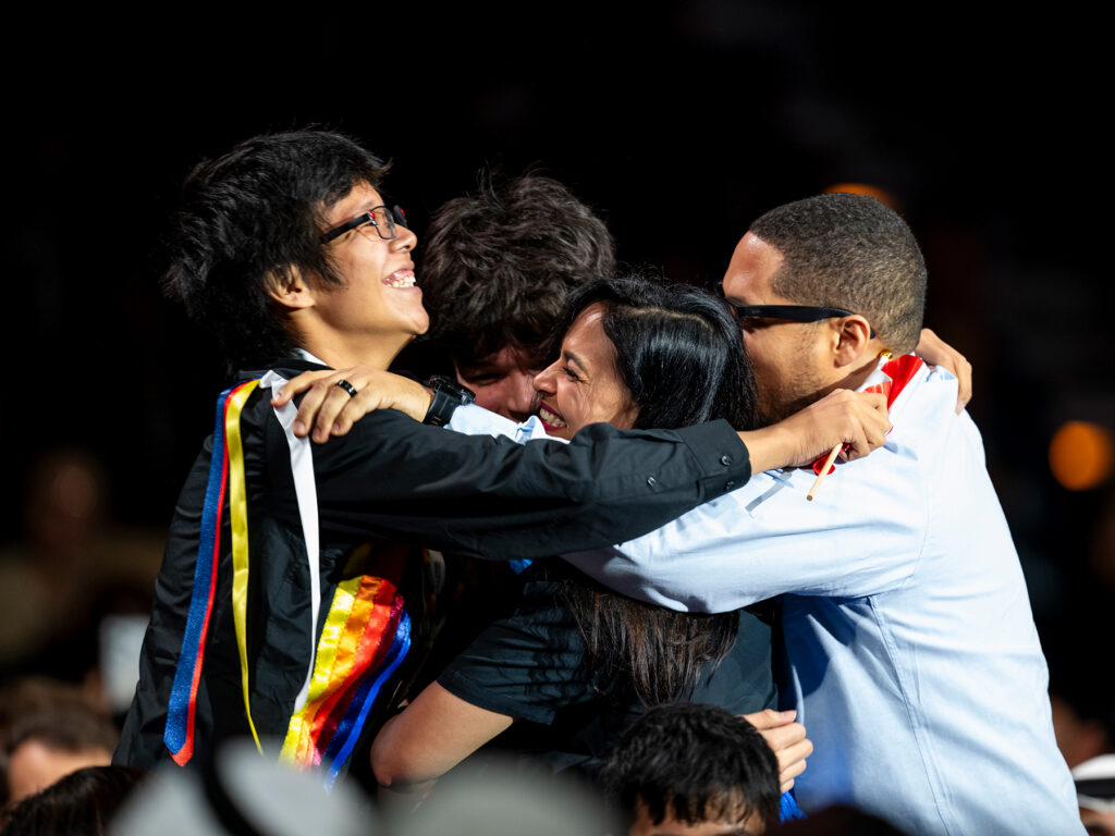 Two teen boys, an adult man and woman smile and hug on a stage
