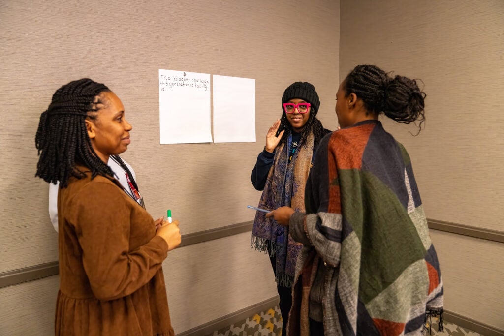 Three women standing in front of two large wall post-its.