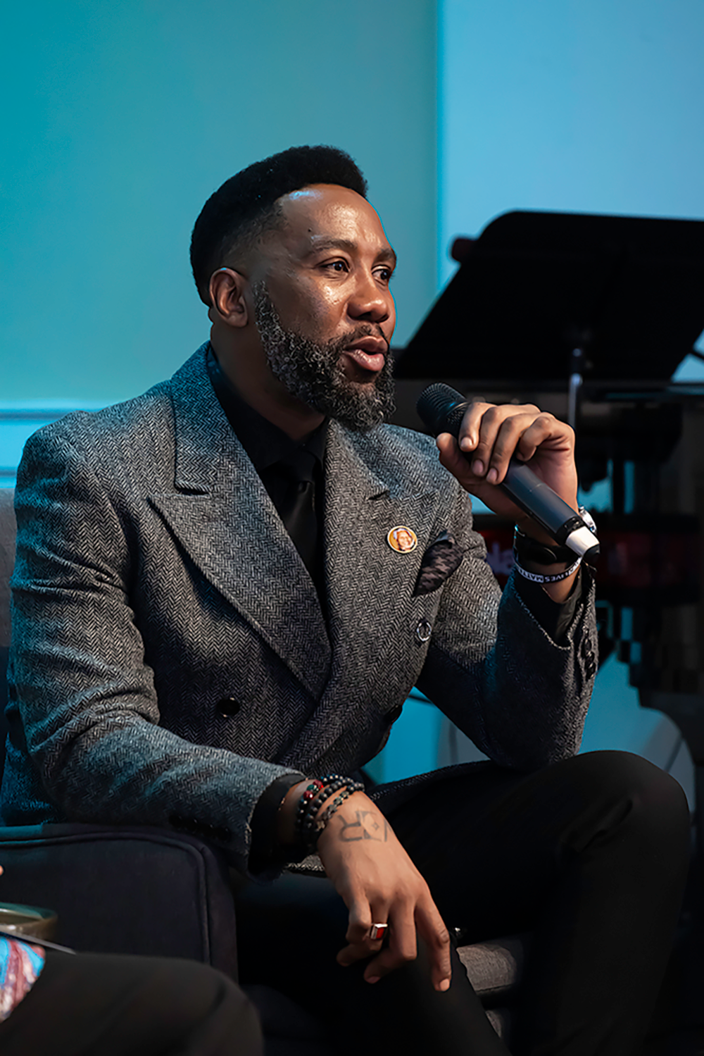 A man seated on a stage speaks into a microphone.