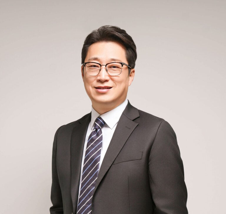 Asian man in a dark suit standing.