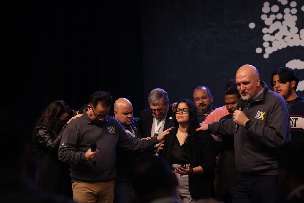 Photo of a group of men and women praying over a woman in the middle.