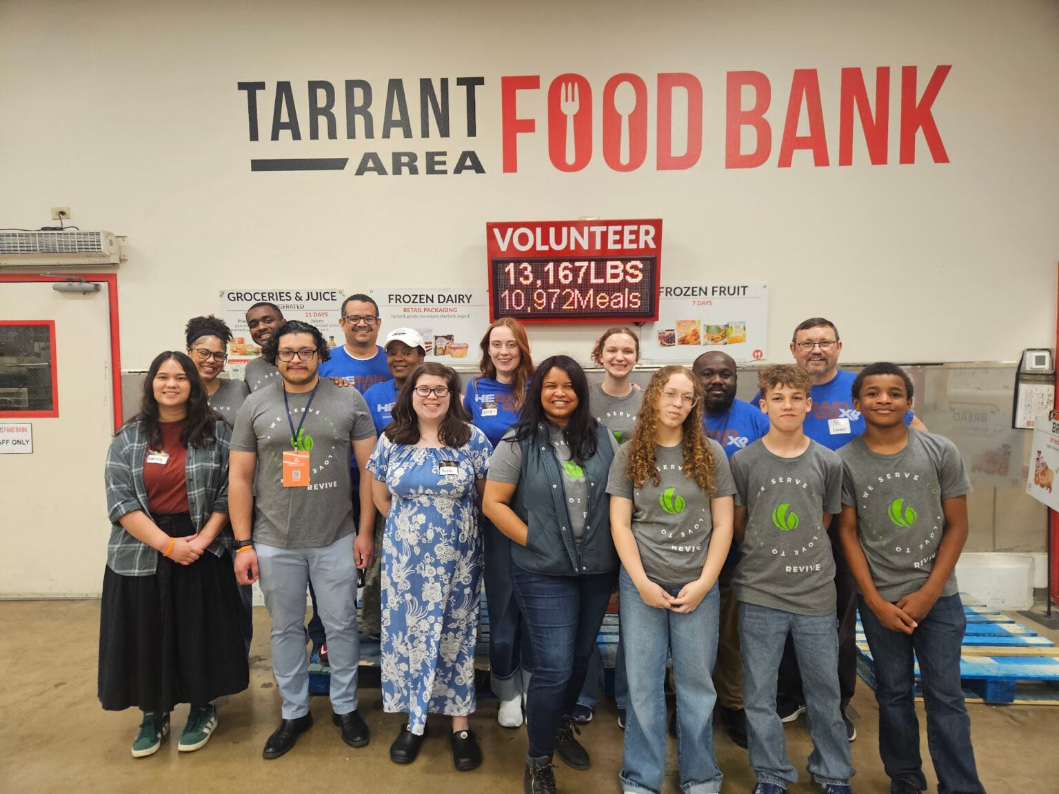 A diverse group of people smile for a photo in front of a wall that reads Tarrant Area Food Bank.