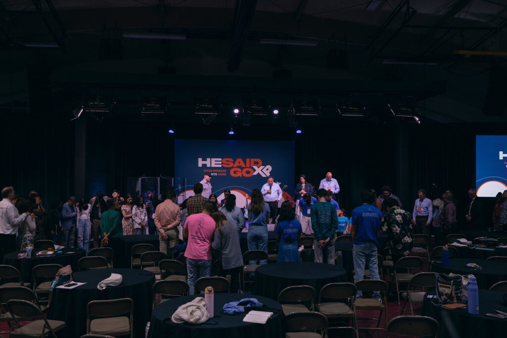 People stand at the front of the room for an altar call at the He Said Go XP Conference.