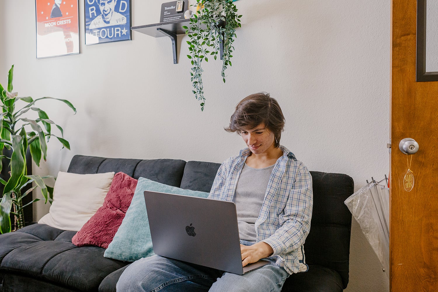 Caucasian male college student sits on sofa with Mac laptop computer.