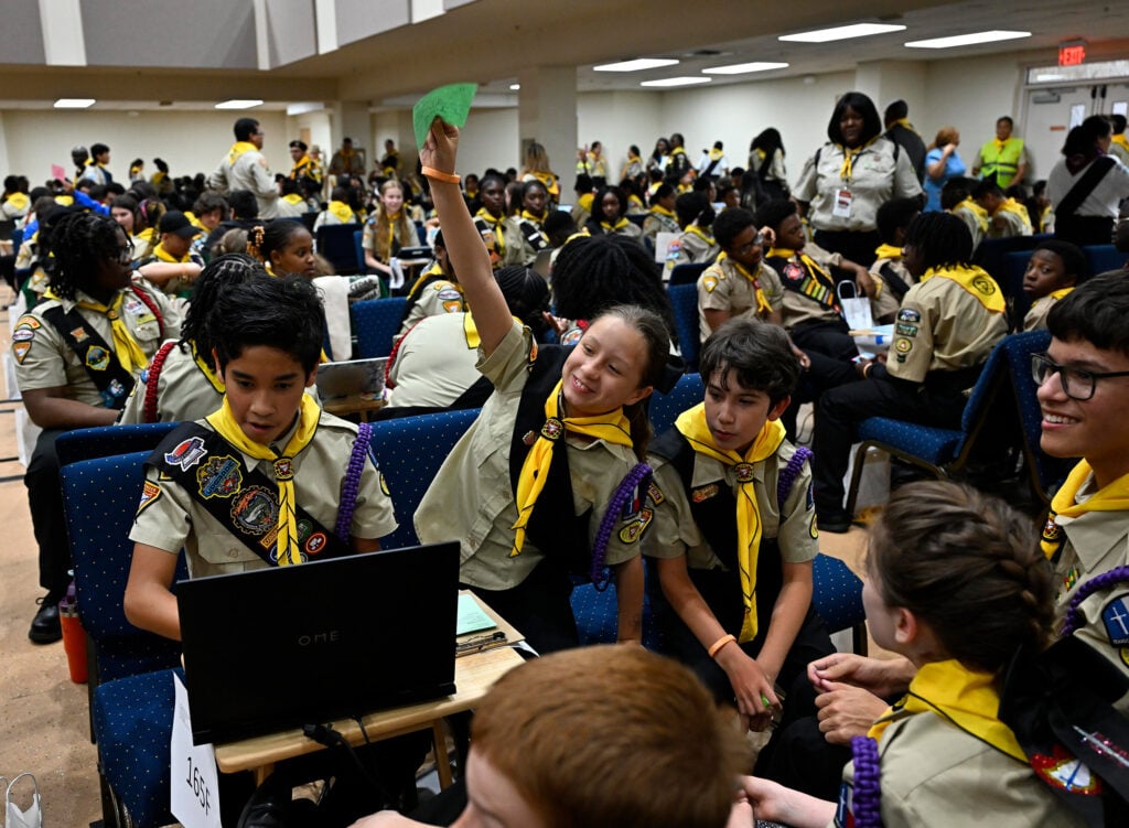 A girl raises her hand with a green piece of paper with an answer written on it on the Pathfinder Bible Experience testing floor. 