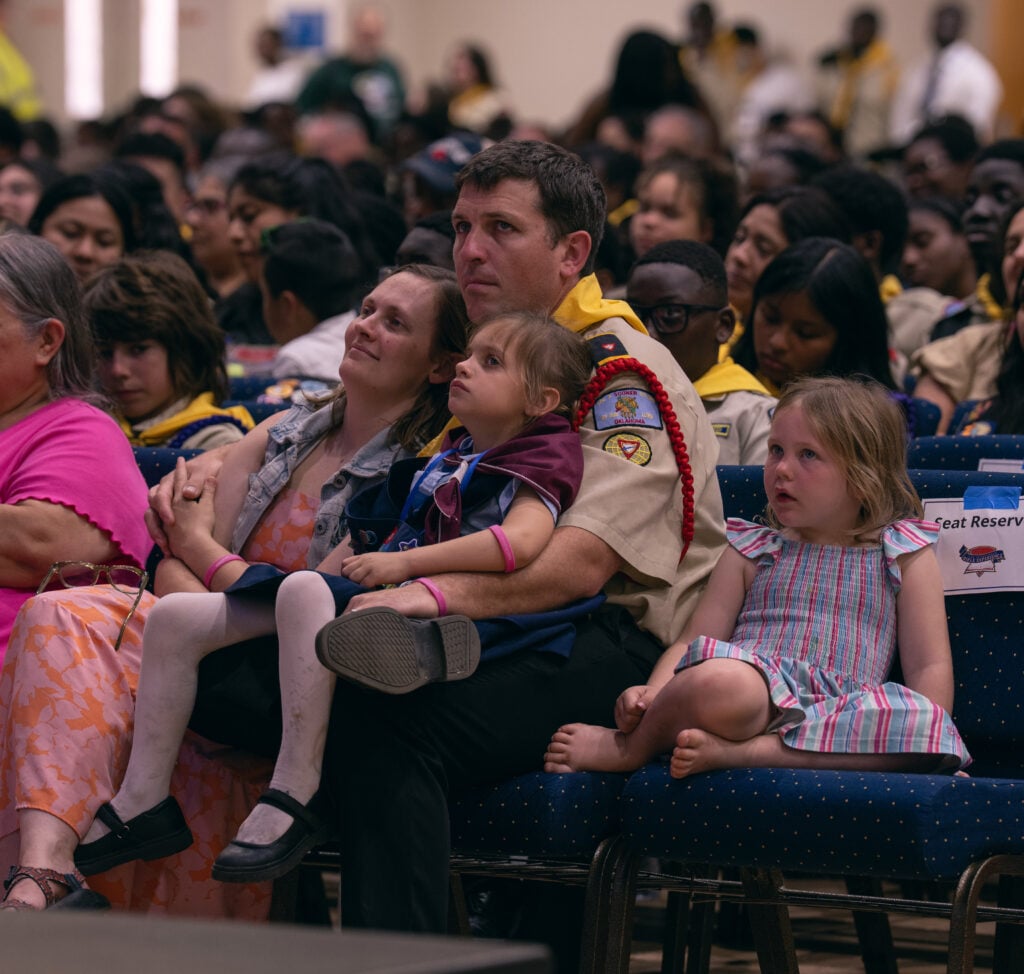 A couple sit in a packed room at Pathfinder Bible Experience with their two daughters. 