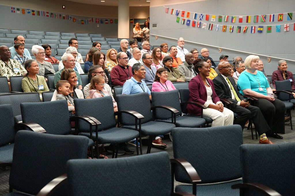Wideshot of a diverse group of people in the NAD auditorium. Plastic flags adorn the wall