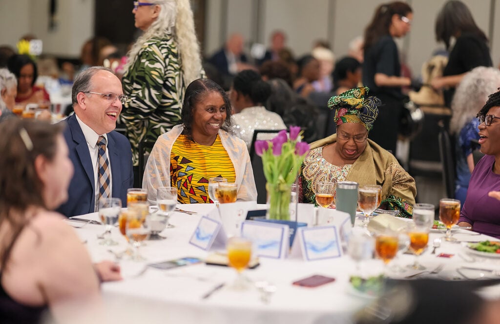 A man and several women laugh around a banque table