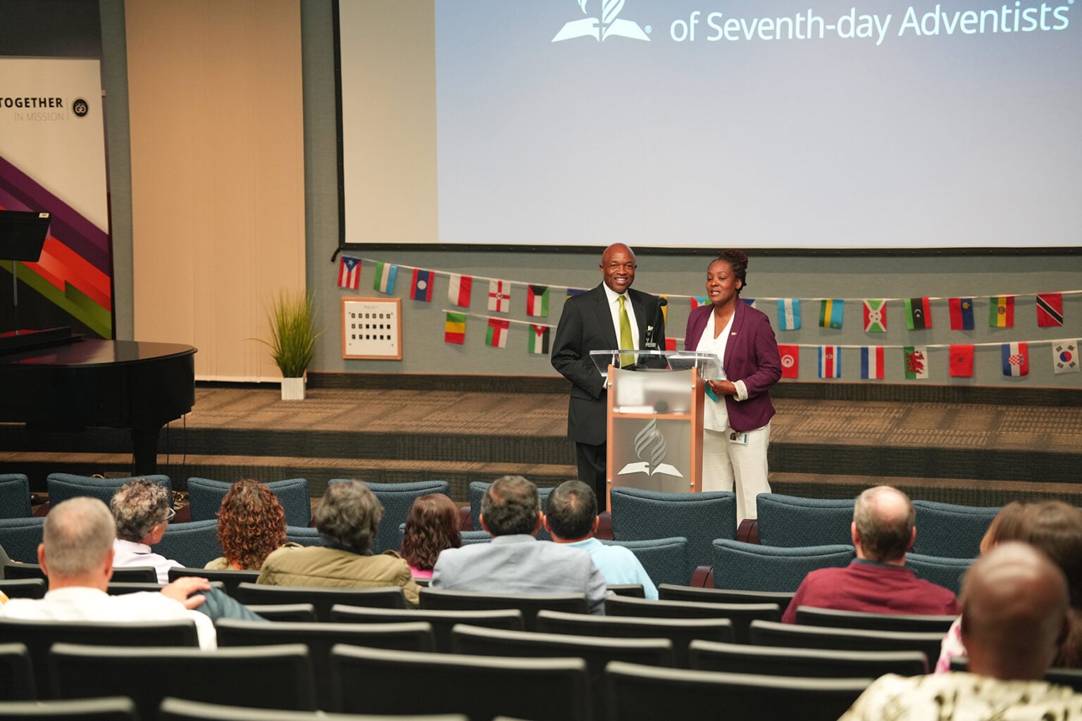 Orna Garnett and G. Alexander Bryant stand behind a podium in front of returning missionaries.