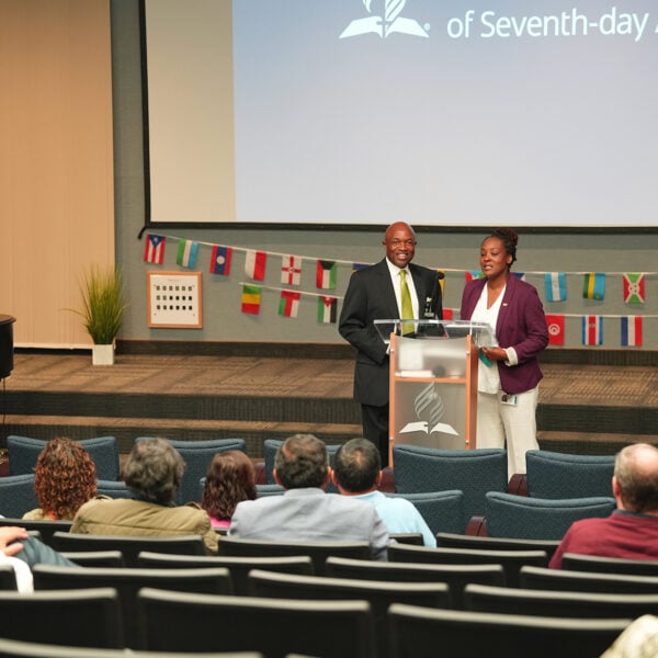 Orna Garnett and G. Alexander Bryant stand behind a podium in front of returning missionaries.