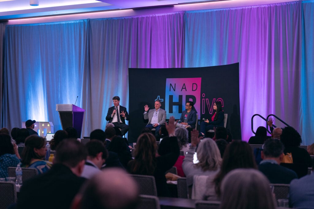 Wide shot of a panel at the front of the HR conference with the audience in foreground