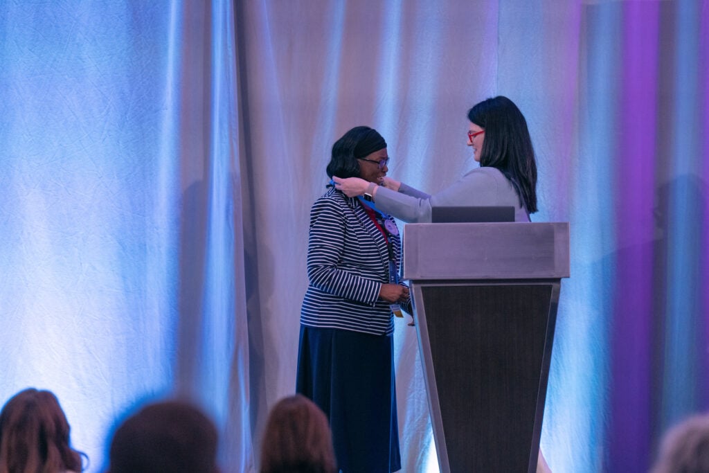 Danielle Toddy places a recognition medal around the neck of HR professional during an awards presentation.