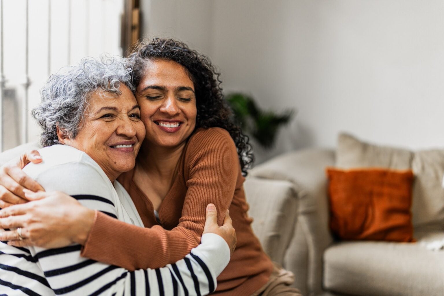 Younger woman hugs older woman in a warm, homelike setting.